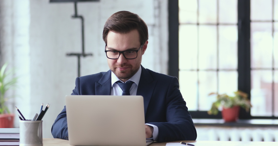Overjoyed young businessman in formal wear and glasses looking at laptop screen, excited by unbelievable good news. Happy emotional executive celebrating receiving attracted investment notification. Royalty-Free Stock Footage #1054279913