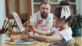 Dad teaching his daughter how to paint. Father's day for father and girl: painting pictures. Young bearded caucasian father and his daughter spending quality time together on special day. - Powered by Shutterstock - Get 15% off with code: PIKWIZARD15