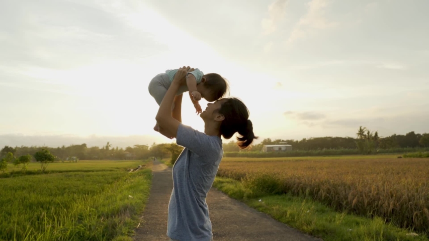 Happy mother and baby playing together outdoor enjoy beautiful sunset in the field