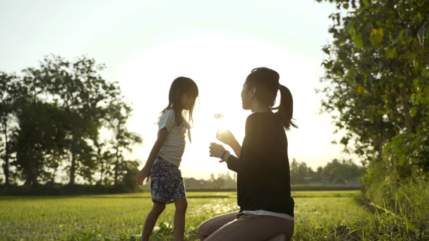 lovely daughter smelling a flower together with mother in the outdoor during sunset