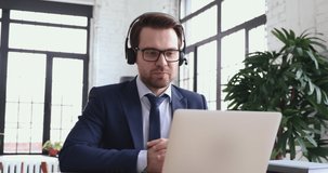Smart male company leader in suit waring headset with mic, holding negotiations talk online with employees, using corporate software in office. Professional lawyer consulting clients by video call.