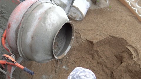 Old dirty concrete-mixer near sand heap at small construction site. Small portable cement mixing machine at home. Building site