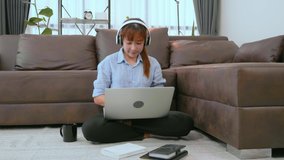 Asian woman is listening to music in headphones dancing while working at home