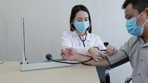 A sliding shot of the female doctor wearing a face mask is measuring the pulse for a middle-aged patient who has a fever and comes to see the doctor at the healthcare center.