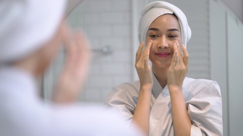 Portrait beautiful young woman looking in mirror at perfect healthy skin touching face with hands after take a bath in bathroom