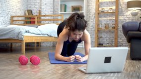20s young Asian woman in sportswear doing plank poses while watching fitness training class on computer laptop online. Healthy girl exercising and learning in bed room. Internet education concept.