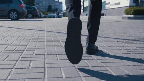 Rear back view feet of businessman commuting to work. Confident guy in leather shoes and suit being on his way to office building
