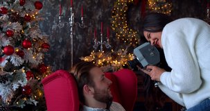 Romantic New Year and Christmas concept. Closeup back view of a white woman holding an old retro film camera for shooting a man, Christmas decorated background. 4k slow motion
