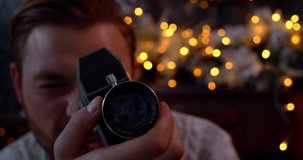 Front view of a white man holding an old retro film camera for shooting, Christmas decorated background. 4k slow motion