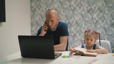 young daughter do homework, sits at table with book, on distance learning, dad sits next, works at computer and talks on phone, say girl not to interfere and not to distract