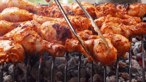 Closeup graded shot of the chicken drumsticks roasting on the charcoal barbecue grill, taken with a macro lens in UHD