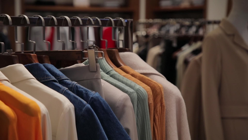 On the hangers are a lot of clothes of various colors. An assortment of women's clothing in a store. Panorama of dresses, jackets, shirts, skirts and other clothes | Shutterstock HD Video #1054307603