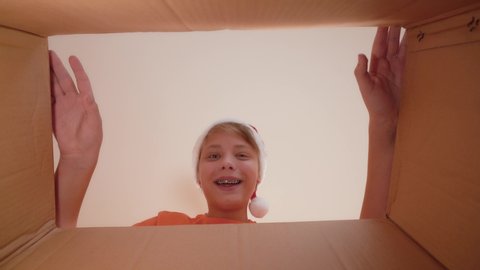 Closeup view video of two curious eyes of young kid looking inside of closed cardboard box through gap than boy opens carton package happily and smiling. Boy happy with his unexpected Christmas gift