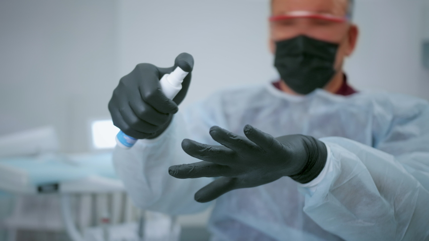 Man in mask is sanitizing hands for fighting coronavirus covid 19 by spraying. Doctor disinfects uniform of corona virus and disinfection by sanitizer is fine. People have disinfectant of Covid-19. | Shutterstock HD Video #1054308794