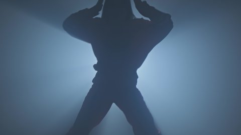 Silhouette of dancer legs walking through dark studio. Young woman entering the stage with smoke on background.Dancing female in 4K, UHD
