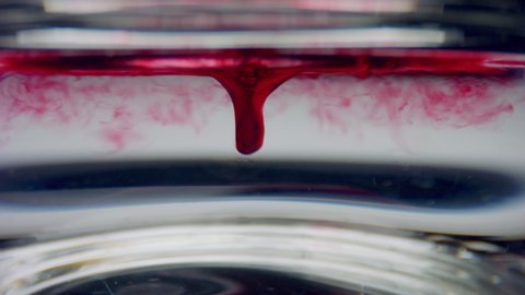 Closeup test tube with blood sample. Clear liquid mixing with red chemical reagent. Macro of blood drops flowing in water. Coronavirus vaccine research in scientific lab