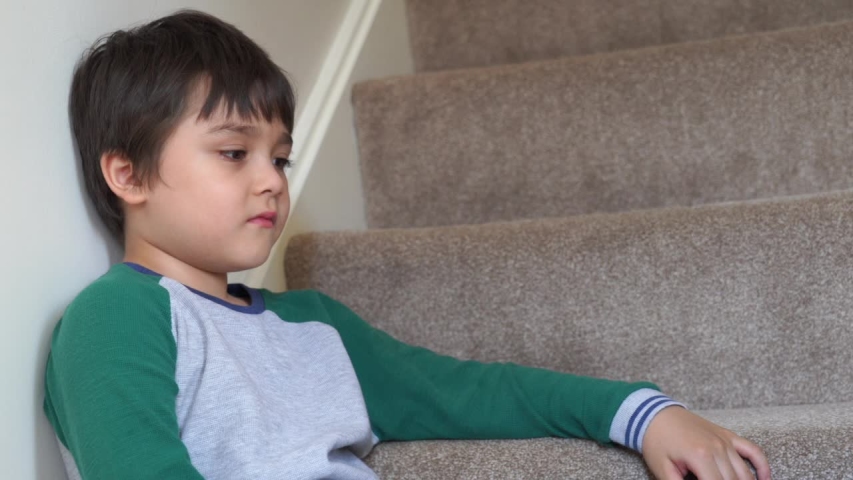 Dramatic portrait of little boy with sad face sitting on stair case, Emotional portrait unhappy kid, Sad child looking down with thinking face, Spoiled childhood, Mental health child concept Royalty-Free Stock Footage #1054317503