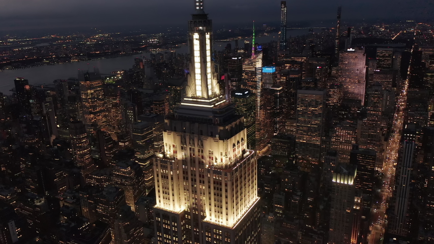 Slow Dolly Slide right Empire State Building in Manhattan at Night surrounded by Skyscrapers in Big City Skyline with City lights flashing, Aerial Drone Shot