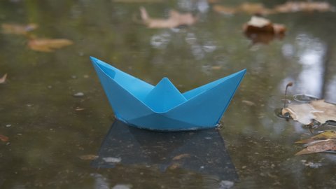 Paper boat in the rain. A blue paper boat in the autumn puddle in the street.