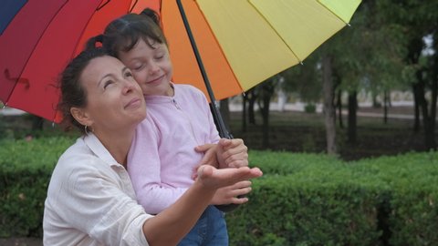 Family under rain drops. Mother stay with her daughter under the colorful umbrella and catch the rain drops in the street.
