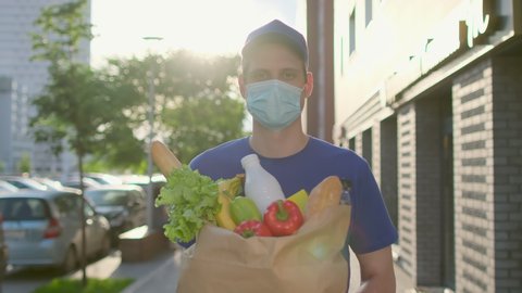 Food Delivery man holding paper bag with food at street outdoors home, deliveryman in protective medical face mask gloves, Coronavirus COVID-19 epidemic quarantine outbreak. Online shopping 4 K slowmo