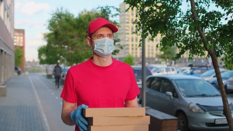 Delivery man holding three pizza cardboard boxes at city street, food deliveryman in protective medical face mask, gloves, Coronavirus COVID-19 epidemic quarantine outbreak. Online shopping 4 K slowmo