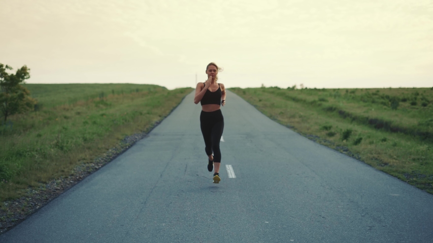 Front Follow up Shot of Girl Athlete Running Alone Down the Road, Getting Ready for a Race Competition or Marathon. Test of Human Endurance. Young Fit Woman in Black Sportswear Jogging Alone. Royalty-Free Stock Footage #1054325573