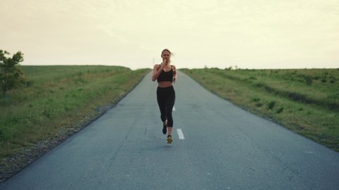 Front Follow up Shot of Girl Athlete Running Alone Down the Road, Getting Ready for a Race Competition or Marathon. Test of Human Endurance. Young Fit Woman in Black Sportswear Jogging Alone.