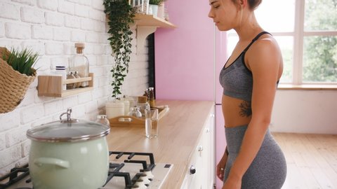 Sporty model taking a bottle of medicine from shelf and takes one pill with water. Home kitchen interior. Dieting, eating disorder, weight loss