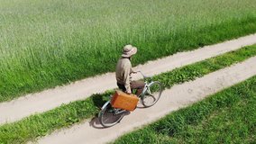 man riding on bicycle by country road in a green field, holding suitcase in a hand, funny travel concept, retro style, aerial shot from drone, top view from above, adventures, happy, creative freedom