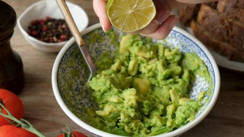 Slow motion of chef squeeze lime into mashed avocado guacamole sauce