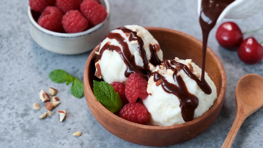 Chocolate pouring on vanolla ice cream scoops. Serving homemade vegetarian ice cream in a bowl with berries, nuts and chocolate syrup Royalty-Free Stock Footage #1054328792