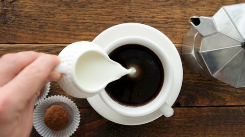 Adding milk to black coffee. Coffee creamer. Coffee with milk on a wooden table top view