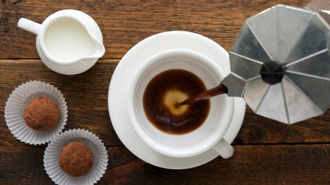 Pouring black coffee in cup. Coffee with chocolate truffles. Cup of black coffee on wooden table