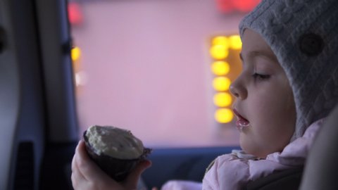 little girl unwraps a cupcake and looks out the car window, slow motion