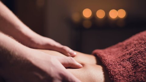 Close-up Young male massage therapist does back massage to a woman with a tattoo in a massage room with dim lights on the background of candles. Low key premium massage concept