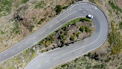 4K Aerial drone rapid footage of small passenger cars passing through curve in mountainous road. Mountain serpentine road, transportation concept, environment concept on Madeira island, Portugal.