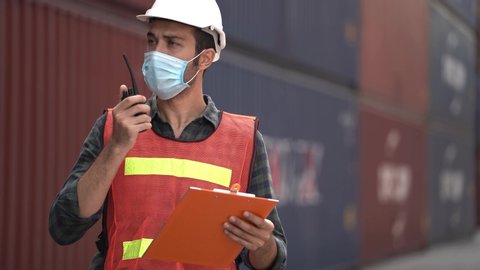 man worker on background of outdoor warehouse cargo container shipping talking on the radio and looking on paper file.