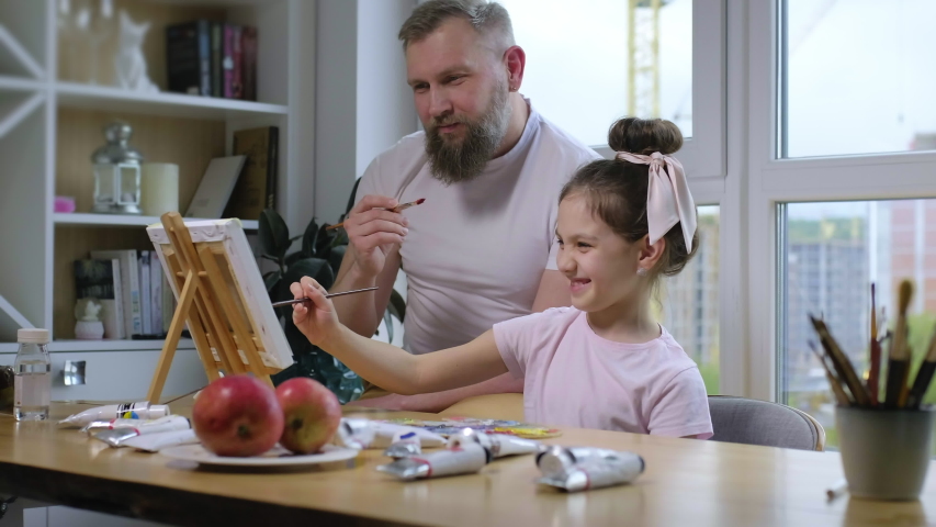 Father and daughter spending quality time together painting pictures: little girl is painting a picture on canvas with her dad. Family time together on Fathers Day. | Shutterstock HD Video #1054332278