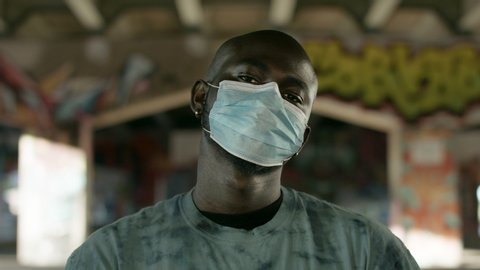A portrait of a black man wearing a medical mask at an urban underpass. Shot in 4k. 