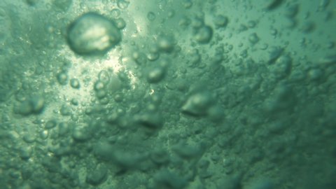 Underwater air Bubbles with sunlight through water surface, natural slow motion under water scene. Air bubbles floating from  the sea bottom up to  water surface