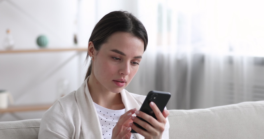Head shot close up displeased young woman looking at smartphone screen, dissatisfied with bad news message, spam or scam sms. Unhappy stressed female mobile app user getting phishing link in email. | Shutterstock HD Video #1054333673