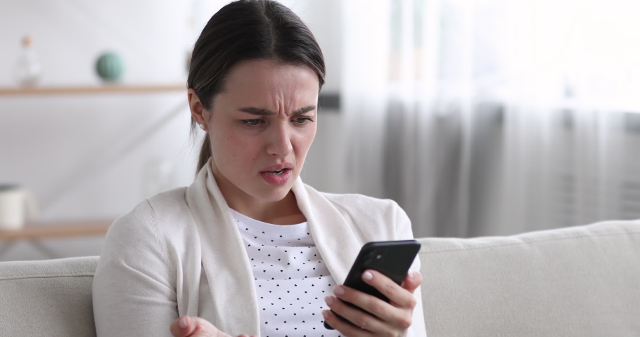 Head shot close up displeased young woman looking at smartphone screen, dissatisfied with bad news message, spam or scam sms. Unhappy stressed female mobile app user getting phishing link in email. | Shutterstock HD Video #1054333673