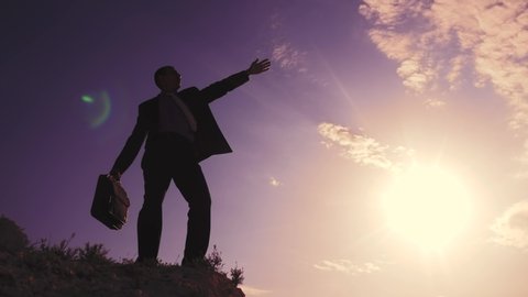 business success teamwork concept. man businessman in jacket with silhouette suitcase rises to the top of the mountain looks into the distance, shows hand direction. manager businessman silhouette