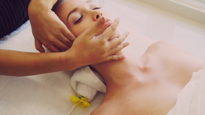 Relaxed woman lying on spa bed for facial and head massage spa treatment by massage therapist in a luxury spa resort. Wellness, stress relief and rejuvenation concept. Royalty-Free Stock Footage #1054336532