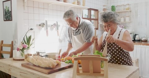 Couple senior Asian elder happy living in home kitchen. Grandfather cooking salad dish with grandmother with happiness and smile enjoy retirement life together. Older people relationship and lifestyle
