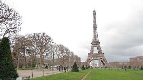The Famous French Metal Eiffel Tower In Paris. European Romantic Symbol Of Love. Distance Shot. Ahead Is Green Grass And A Romantic Park. Day, Cloudy Weather