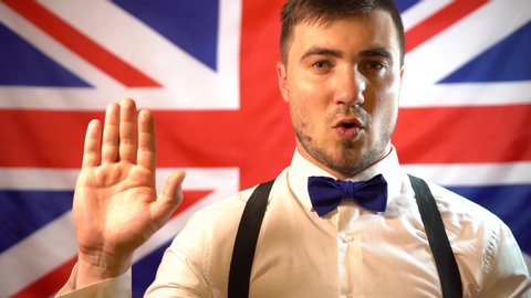 A patriotic British man, a British politician, on the background of the flag of Great Britain, takes the oath with his arm extended forward. British politician swears an oath