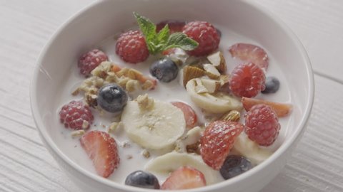 Freshly prepared healthy dieting breakfast from natural organic ingredients fruits, berries, granola and milk in a ceramic bowl and spoon is taking diet food. Slow motion, 2K video, 240fps, 1080p.