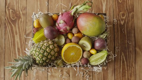 Variety tropical fruits on a wooden straw in a box on a wwoden background. Girl's hands take out ananas, mango, dradon fruit from the box n a table. Fast motion, 4K UHD video, 3840, 2160p.